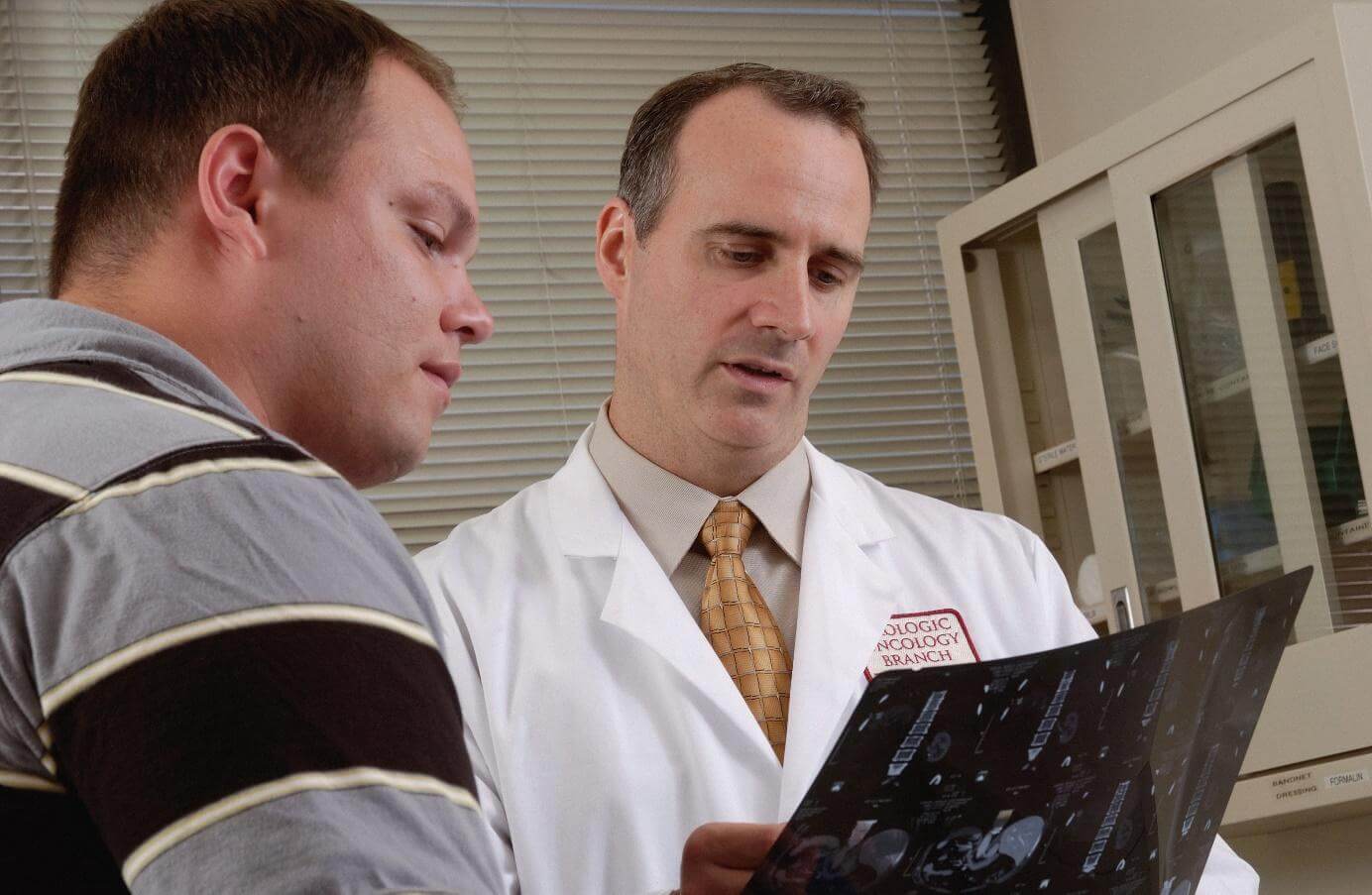 Ein Arzt in einem weißen Kittel zeigt und erklärt einem Patienten ein MRT-Bild in einer medizinischen Einrichtung.